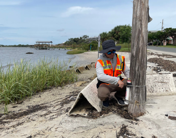 UW undergraduate student Kandai Shimada checking a wave gauge on a wooden pole on the shore